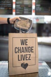 Clean Eatz takeout bag printed with "We Change Livez" on a café table